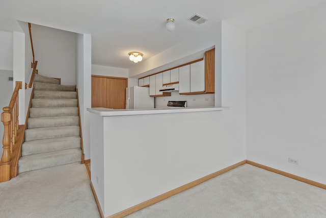 kitchen featuring white fridge, white cabinetry, and light carpet