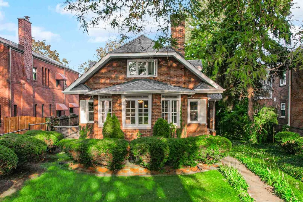 back of property with brick siding, a chimney, fence, and a lawn