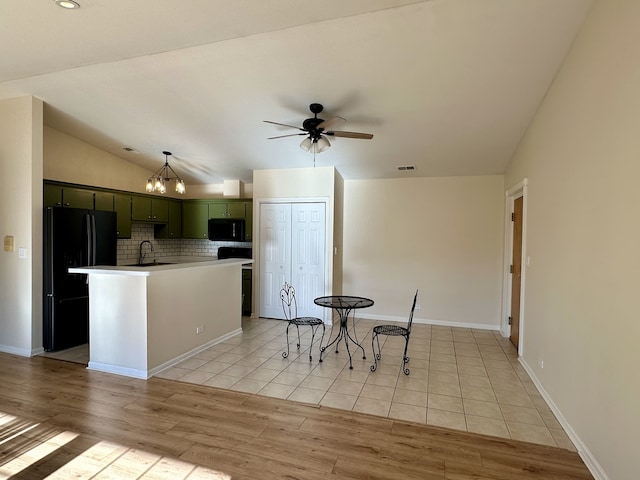 kitchen featuring light hardwood / wood-style flooring, an island with sink, lofted ceiling, black appliances, and green cabinetry