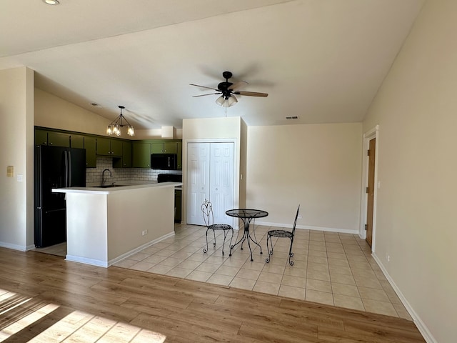 kitchen with light wood-type flooring, green cabinets, black appliances, a center island with sink, and lofted ceiling