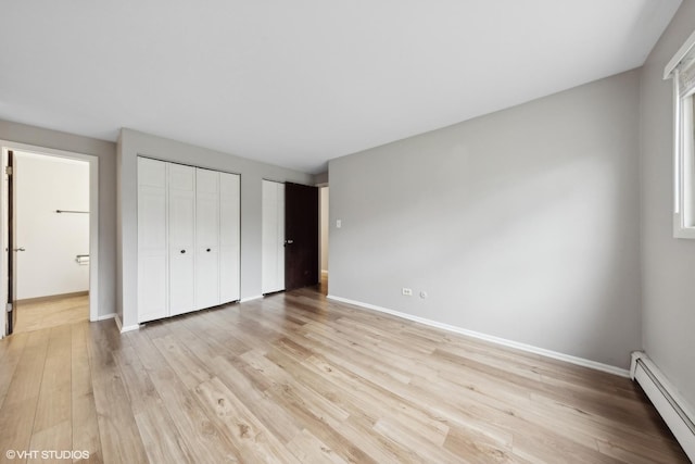 unfurnished bedroom with two closets, baseboard heating, and light hardwood / wood-style floors