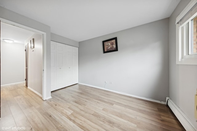 unfurnished bedroom featuring a baseboard radiator, a closet, and light hardwood / wood-style flooring