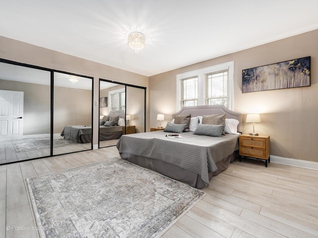 bedroom featuring light wood-style flooring, baseboards, and multiple closets