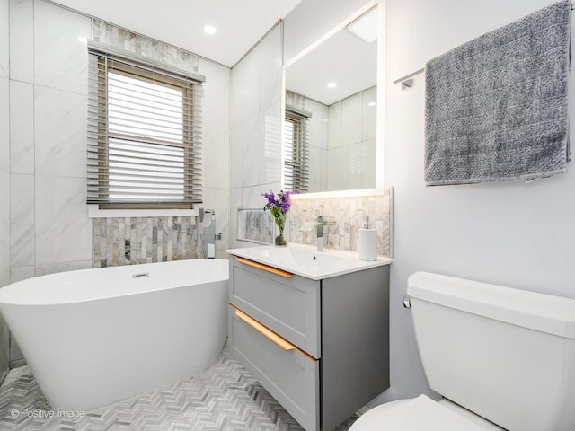 full bathroom with toilet, a freestanding bath, vanity, tile walls, and recessed lighting