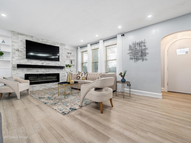 living room featuring light wood finished floors, baseboards, arched walkways, built in features, and a fireplace