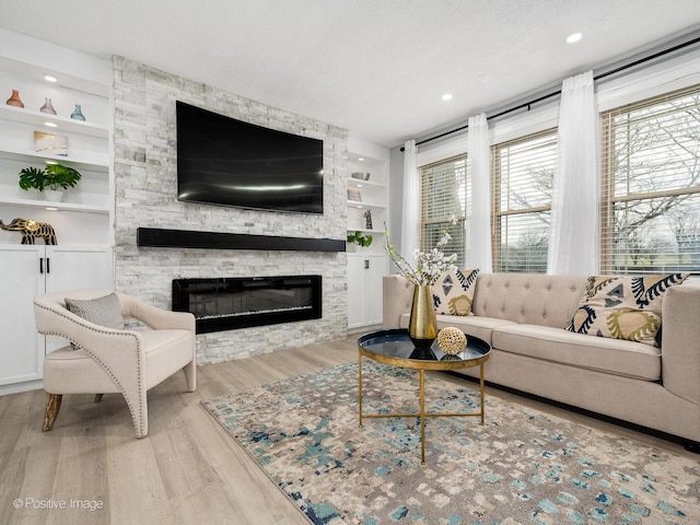 living area with a textured ceiling, a stone fireplace, built in shelves, recessed lighting, and light wood-type flooring