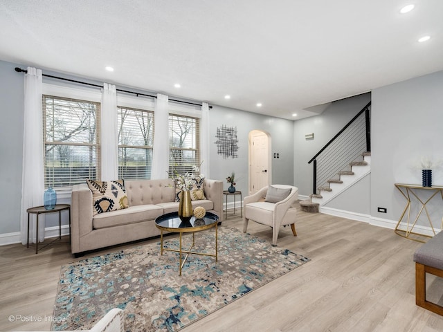 living room with arched walkways, baseboards, light wood finished floors, and stairs