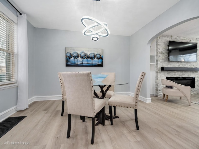 dining space with an inviting chandelier, a fireplace, baseboards, and light wood finished floors