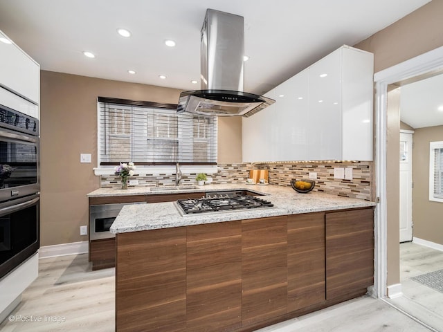 kitchen with modern cabinets, stainless steel gas stovetop, white cabinets, island range hood, and light stone countertops