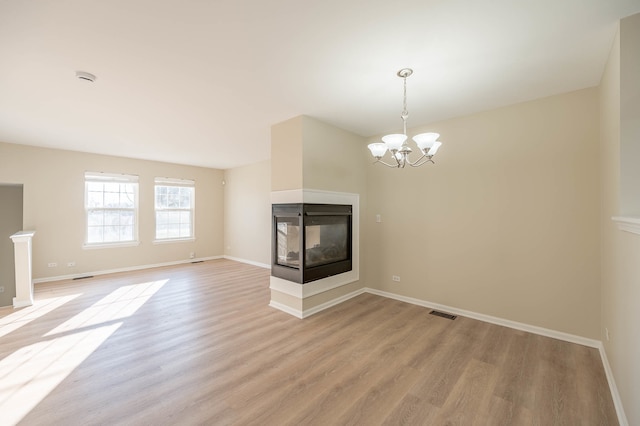 unfurnished living room with a notable chandelier, a multi sided fireplace, and light hardwood / wood-style flooring