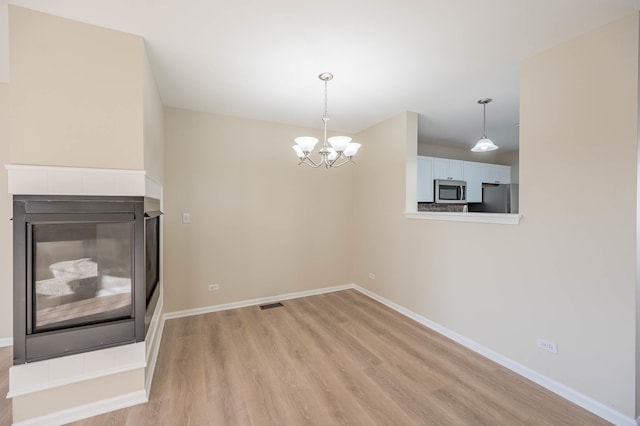 unfurnished dining area featuring a chandelier, a multi sided fireplace, and light hardwood / wood-style flooring