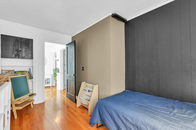 bedroom with wooden walls, light hardwood / wood-style flooring, and ornamental molding