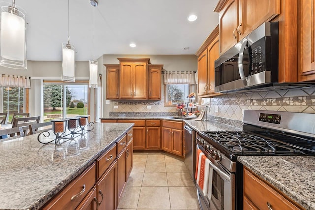 kitchen featuring light stone countertops, tasteful backsplash, stainless steel appliances, decorative light fixtures, and light tile patterned flooring