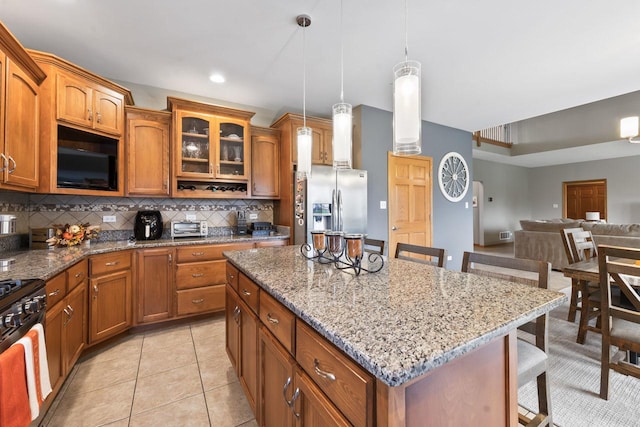 kitchen with a center island, stainless steel fridge, decorative light fixtures, a breakfast bar area, and black microwave