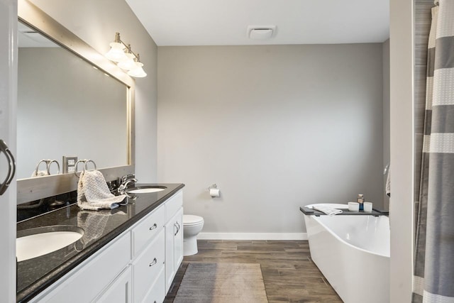 bathroom featuring a tub, hardwood / wood-style floors, vanity, and toilet