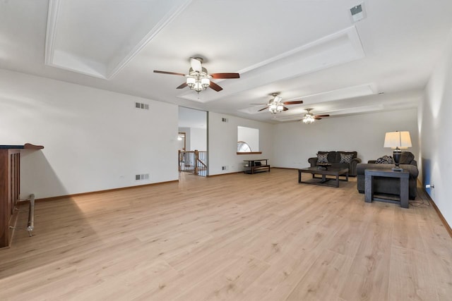 living room with a tray ceiling, ceiling fan, and light wood-type flooring