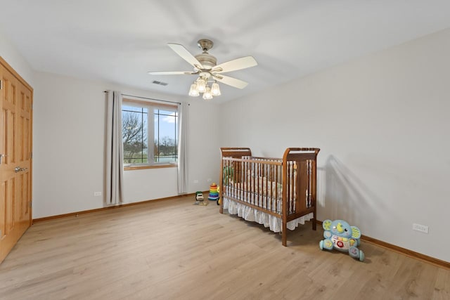 bedroom with a crib, light hardwood / wood-style flooring, and ceiling fan