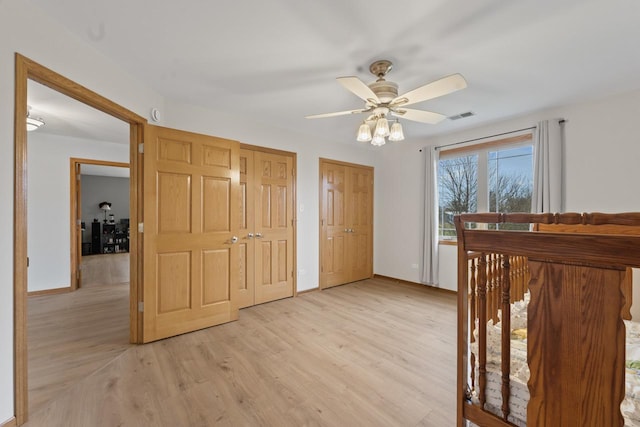 unfurnished bedroom featuring two closets, ceiling fan, and light hardwood / wood-style floors