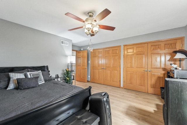 bedroom featuring light wood-type flooring, ceiling fan with notable chandelier, and two closets