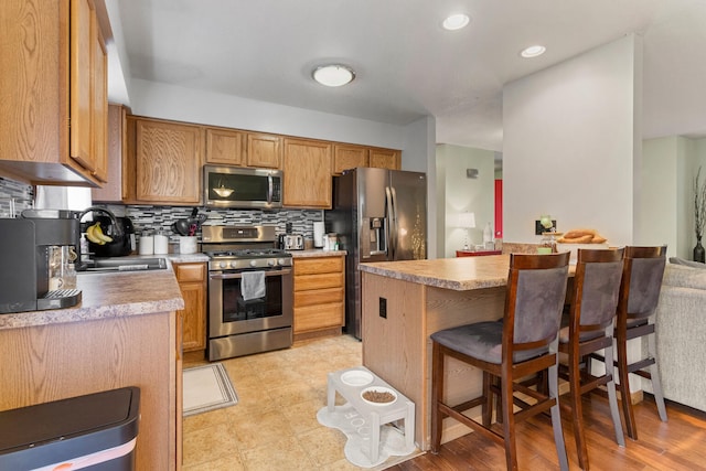 kitchen featuring sink, stainless steel appliances, a kitchen breakfast bar, tasteful backsplash, and light wood-type flooring