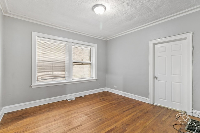 empty room with visible vents, crown molding, a textured ceiling, and wood finished floors