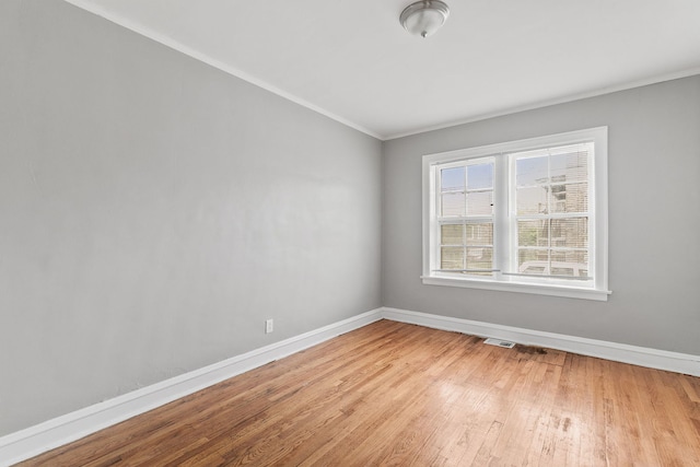 spare room with light wood finished floors, visible vents, baseboards, and ornamental molding
