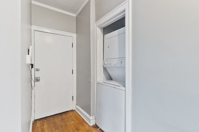washroom with crown molding, stacked washer / drying machine, and wood finished floors