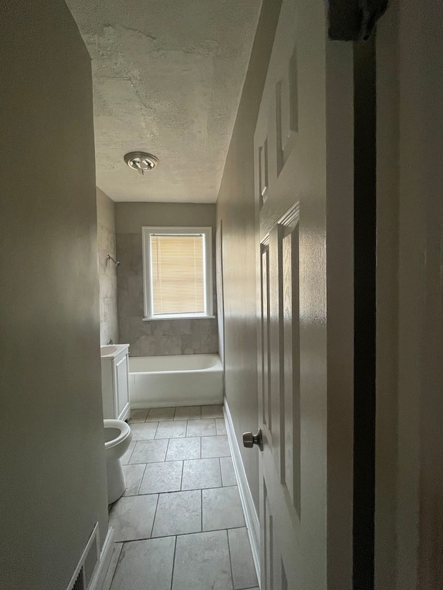 bathroom featuring tile patterned floors, toilet, a textured ceiling, and tiled shower / bath