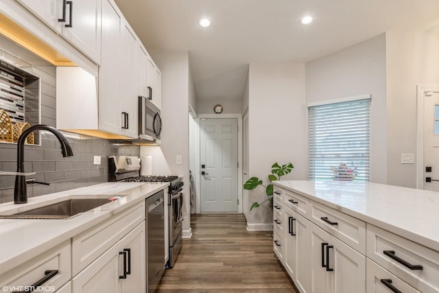 kitchen with sink, light stone counters, white cabinets, stainless steel appliances, and backsplash