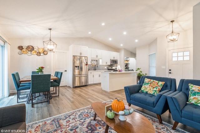 living room featuring vaulted ceiling, sink, a notable chandelier, and light hardwood / wood-style floors