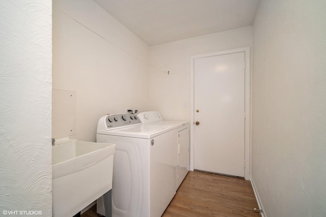 clothes washing area featuring sink, washer and clothes dryer, and wood-type flooring