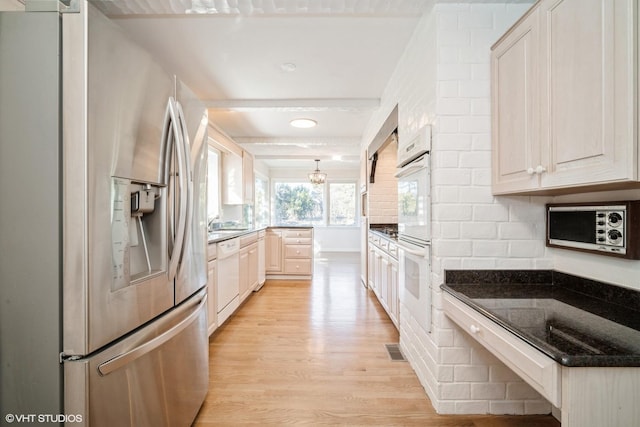 kitchen with tasteful backsplash, light wood-type flooring, stainless steel fridge, dishwasher, and dark stone counters