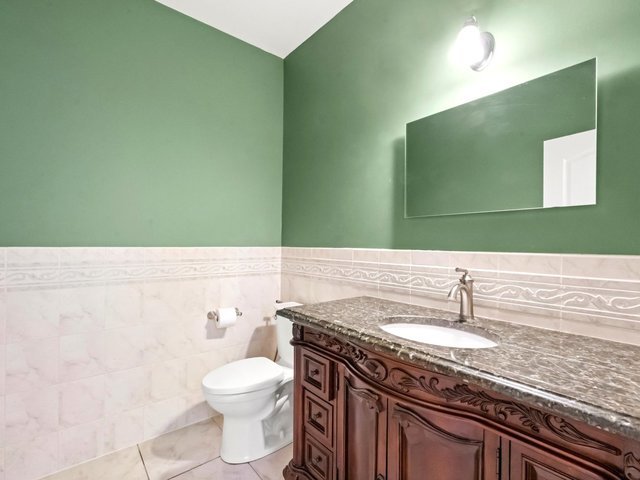 bathroom with toilet, vanity, tile patterned floors, and tile walls