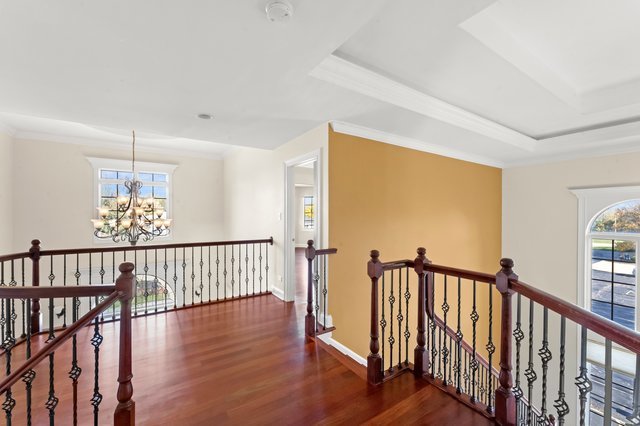 hallway with a raised ceiling, crown molding, dark wood-type flooring, and an inviting chandelier