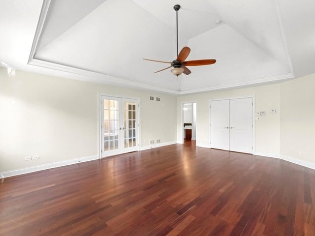 unfurnished living room with ceiling fan, a raised ceiling, dark wood-type flooring, and french doors