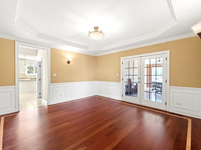 spare room featuring a raised ceiling, wood-type flooring, a wealth of natural light, and french doors