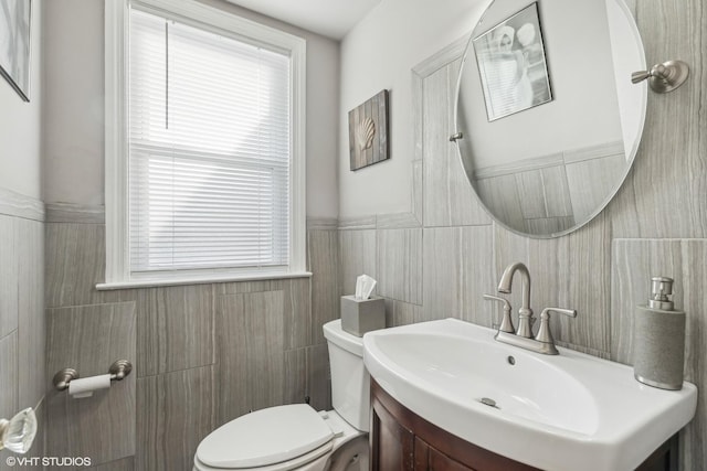 bathroom with a wealth of natural light, vanity, tile walls, and toilet