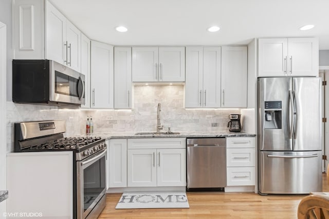 kitchen with light stone countertops, sink, stainless steel appliances, backsplash, and white cabinets