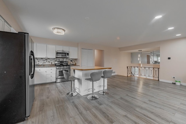 kitchen featuring appliances with stainless steel finishes, a breakfast bar, decorative light fixtures, white cabinets, and light hardwood / wood-style floors