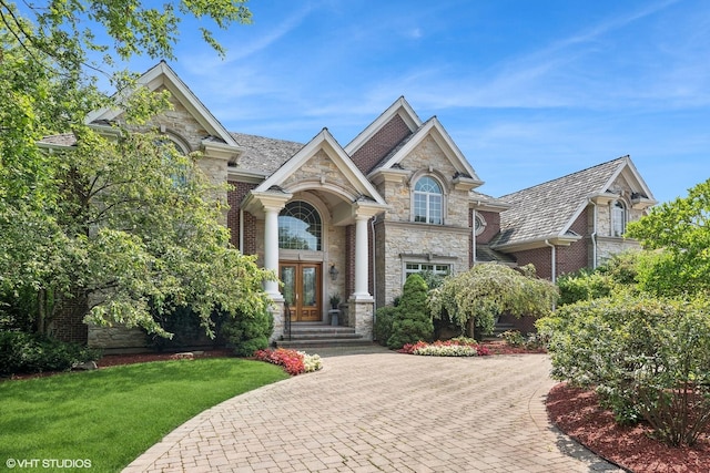 view of front of property with a front yard, french doors, stone siding, decorative driveway, and brick siding