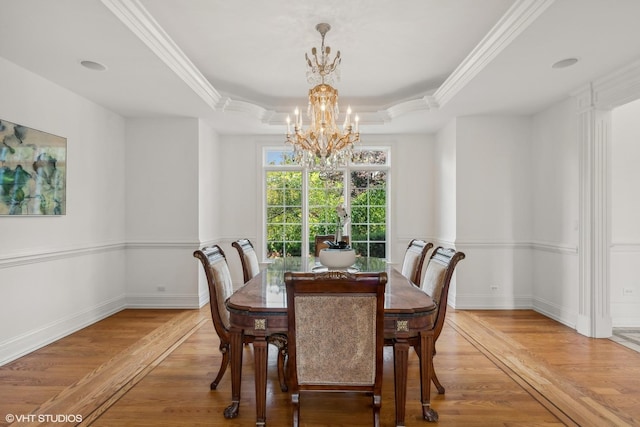 dining space featuring a raised ceiling, light wood-style floors, an inviting chandelier, and ornamental molding