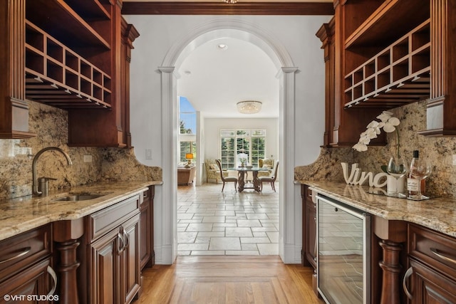 kitchen with open shelves, a sink, wine cooler, arched walkways, and light stone countertops