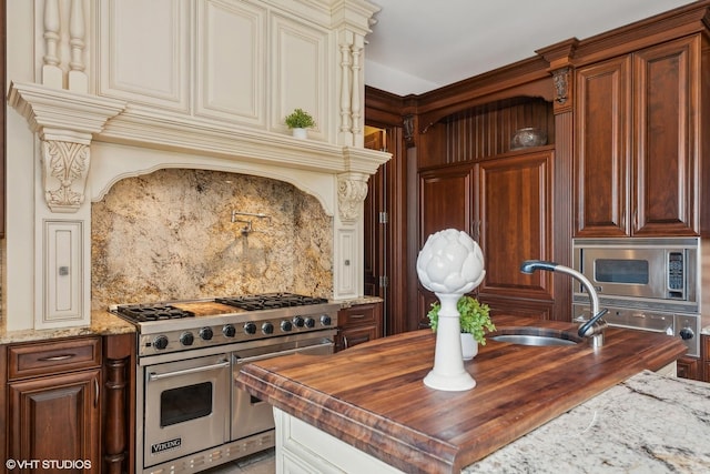 kitchen with a sink, butcher block countertops, cream cabinetry, appliances with stainless steel finishes, and tasteful backsplash