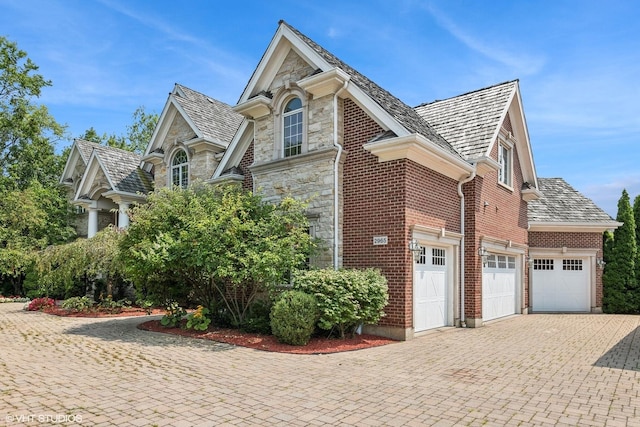 view of side of property featuring decorative driveway, stone siding, brick siding, and a garage