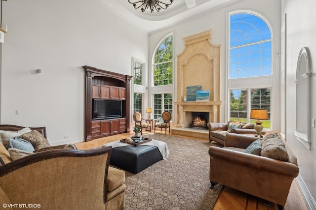 living area featuring light wood finished floors, a healthy amount of sunlight, crown molding, a premium fireplace, and a towering ceiling