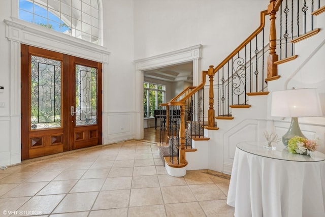 foyer featuring light tile patterned flooring, stairs, a towering ceiling, wainscoting, and a decorative wall