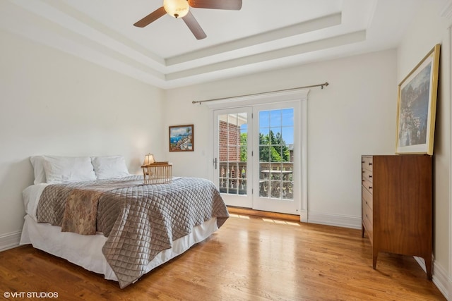 bedroom featuring wood finished floors, a raised ceiling, baseboards, and access to outside