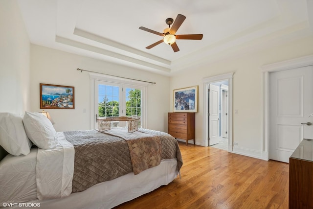 bedroom with a ceiling fan, baseboards, a raised ceiling, access to outside, and light wood-type flooring