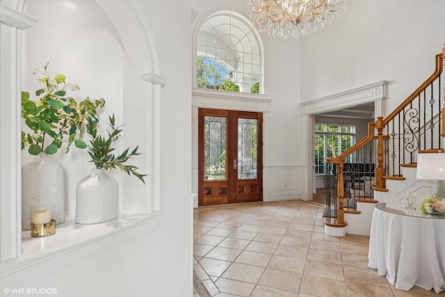 foyer entrance with a high ceiling, light tile patterned flooring, stairs, wainscoting, and a notable chandelier