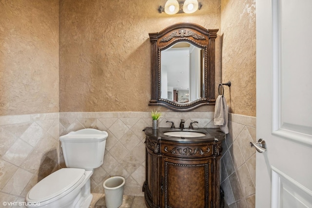 bathroom featuring tile walls, toilet, wainscoting, a textured wall, and vanity